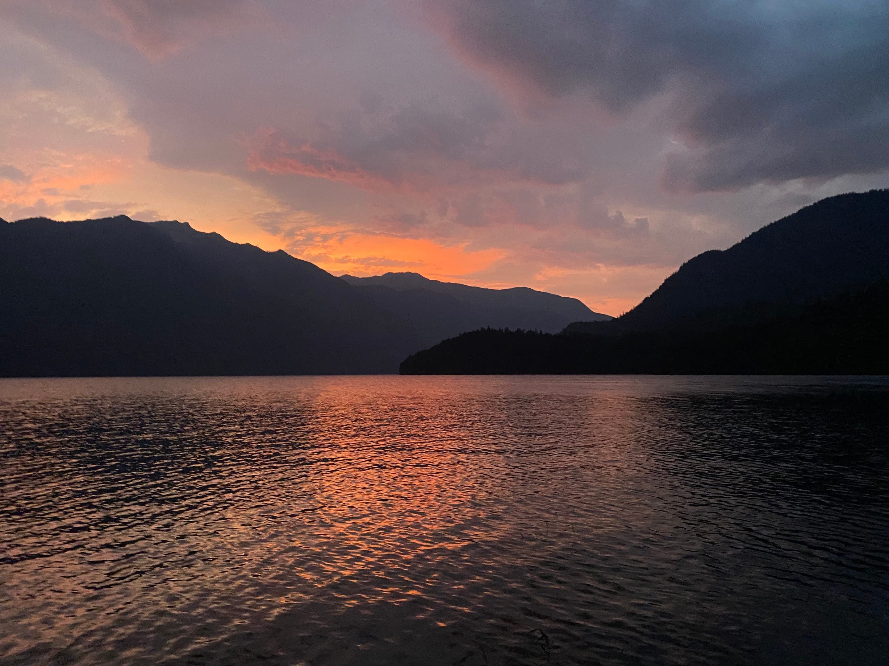 Sunset over a lake framed by dark mountain silhouettes.