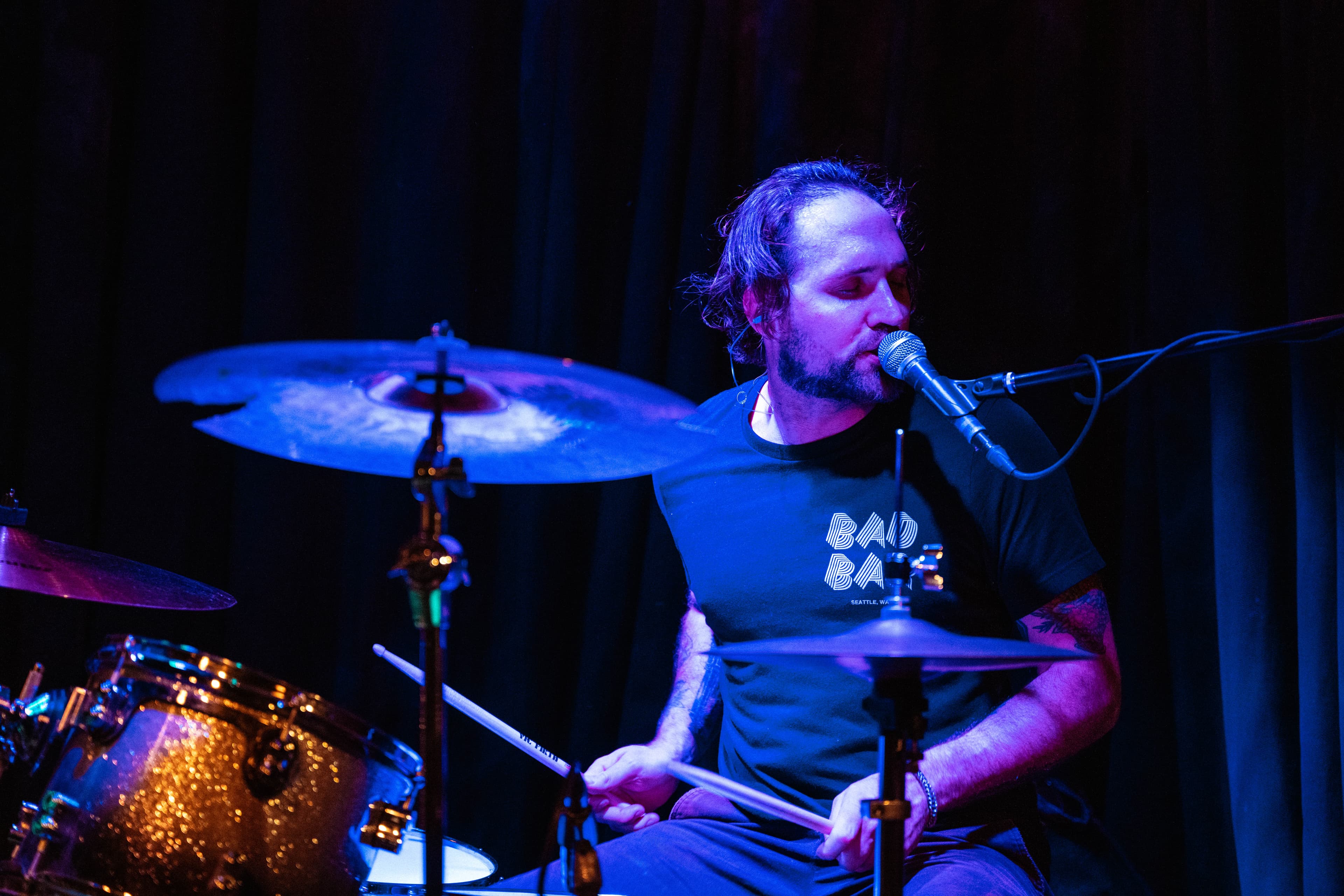 Elliot Preston singing at the drums with Blade Palace under blue stage lights.