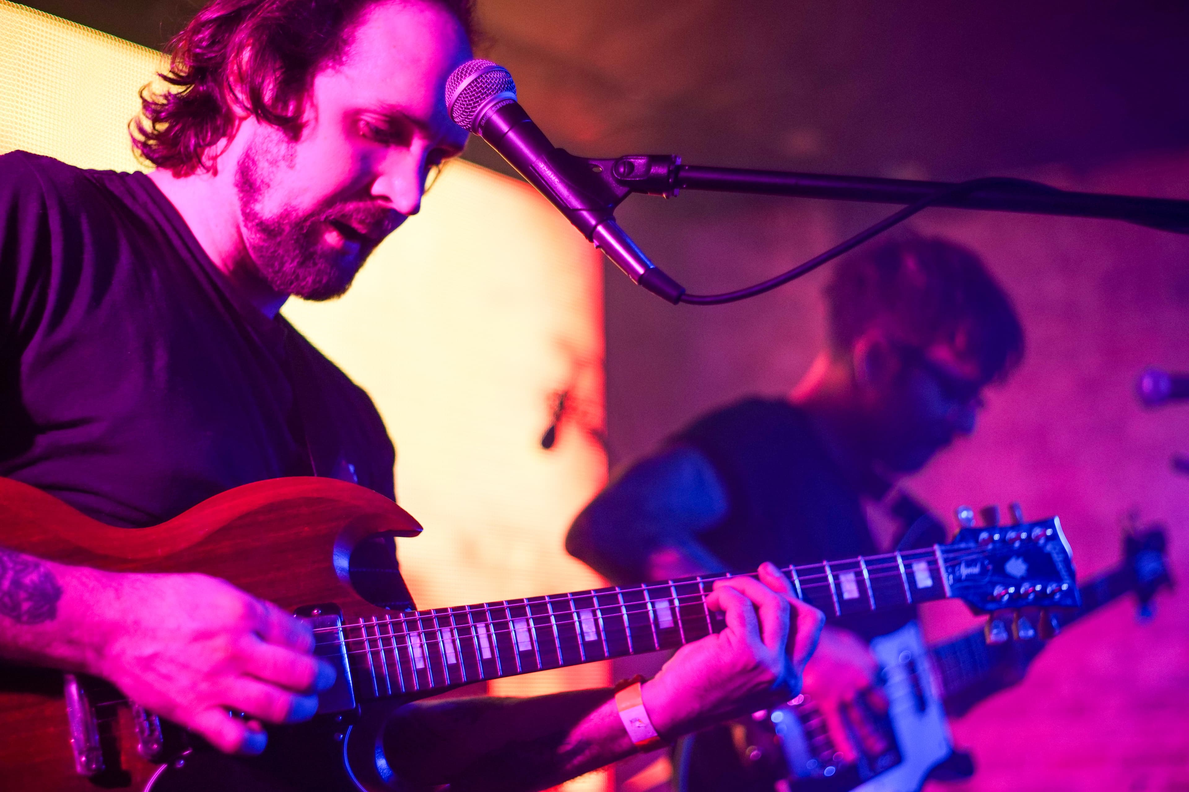 Elliot Preston playing guitar with Peyote Ugly under pink stage lights.
