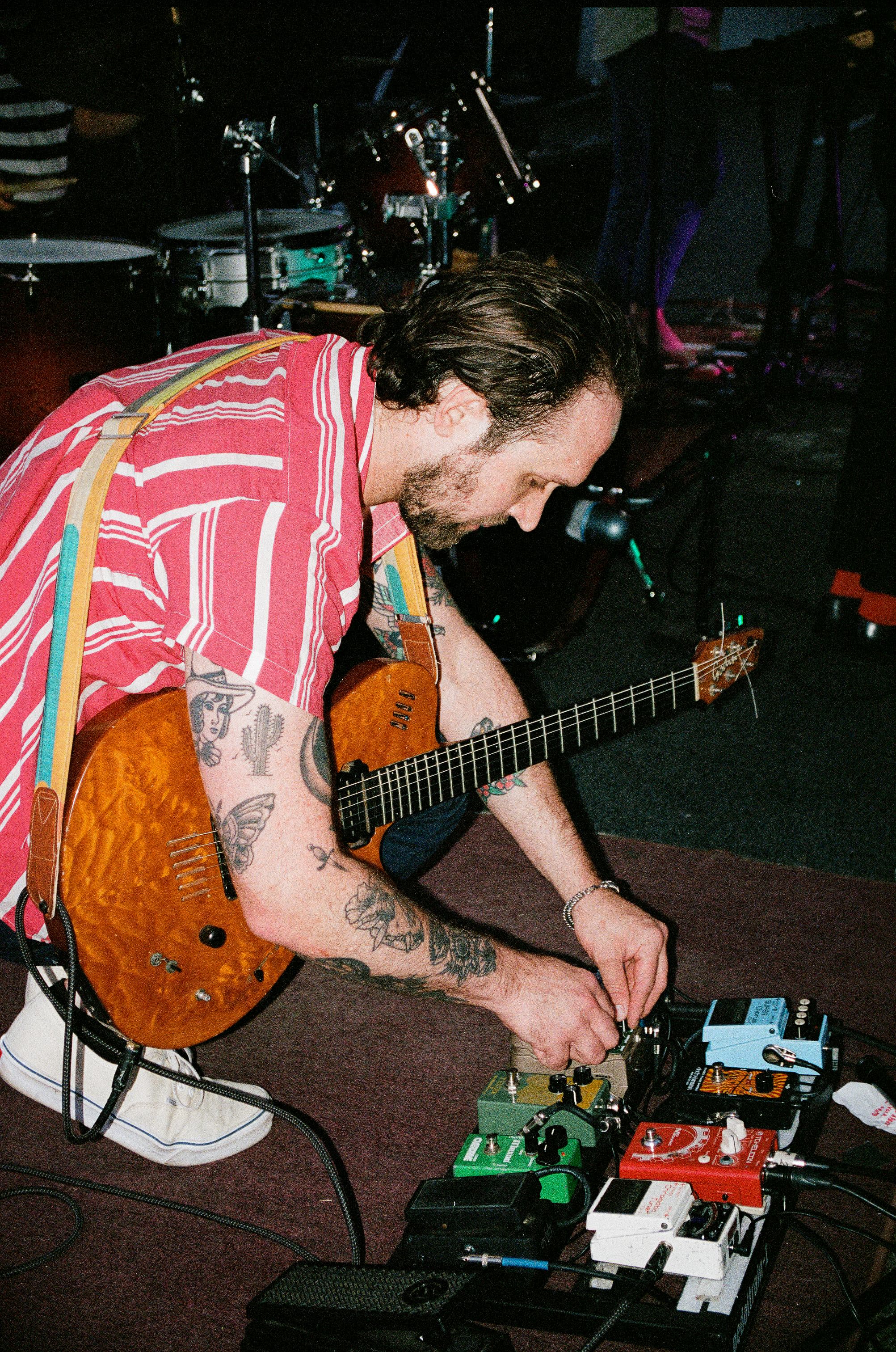 Elliot Preston adjusting effects pedals with a guitar across his lap.