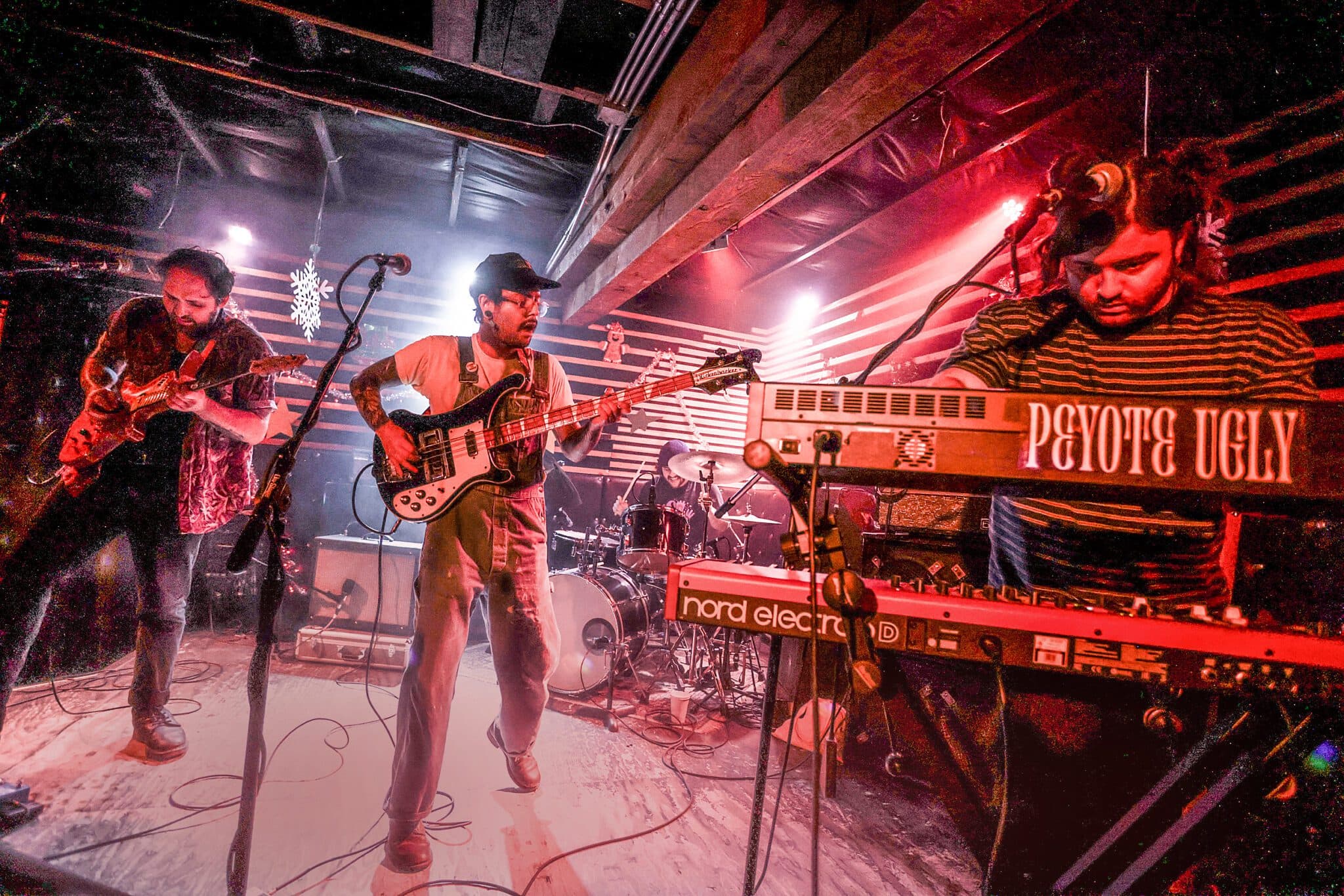 Peyote Ugly performing live with guitar, bass, drums, and keyboards under red stage lights.